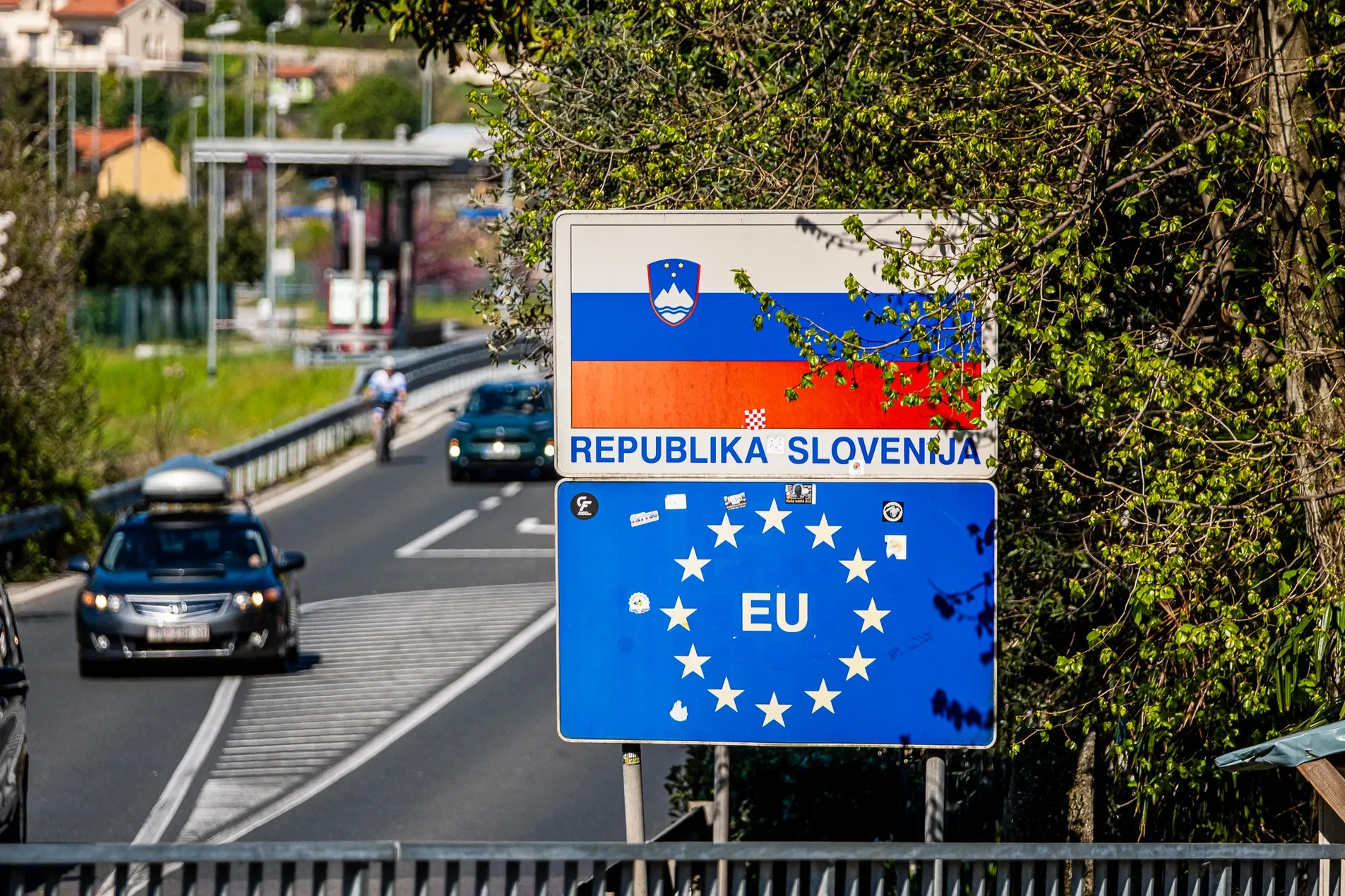 Republika Slovenija entry sign with Slovenian flag, coat of arms and EU sign at Dragonja border crossing with cars and cyclist passing on a sunny spring day, April 2026
