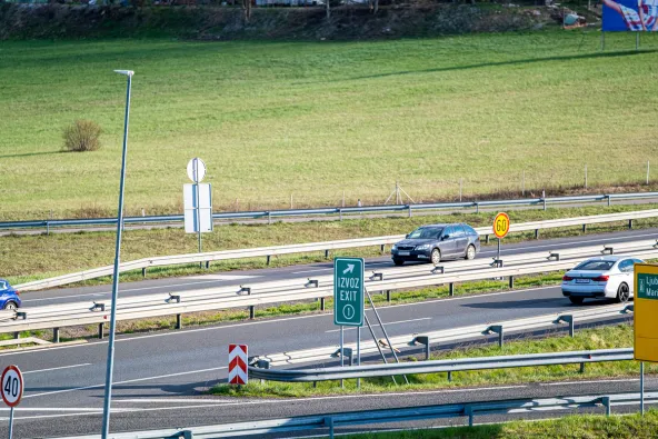 Slovenia motorway exit sign reading Izvoz Exit 1 with directional arrow, 60 km/h speed limit sign, cars on A1 motorway near Maribor with green fields and Ljubljana–Maribor direction sign partially visible, April 2026